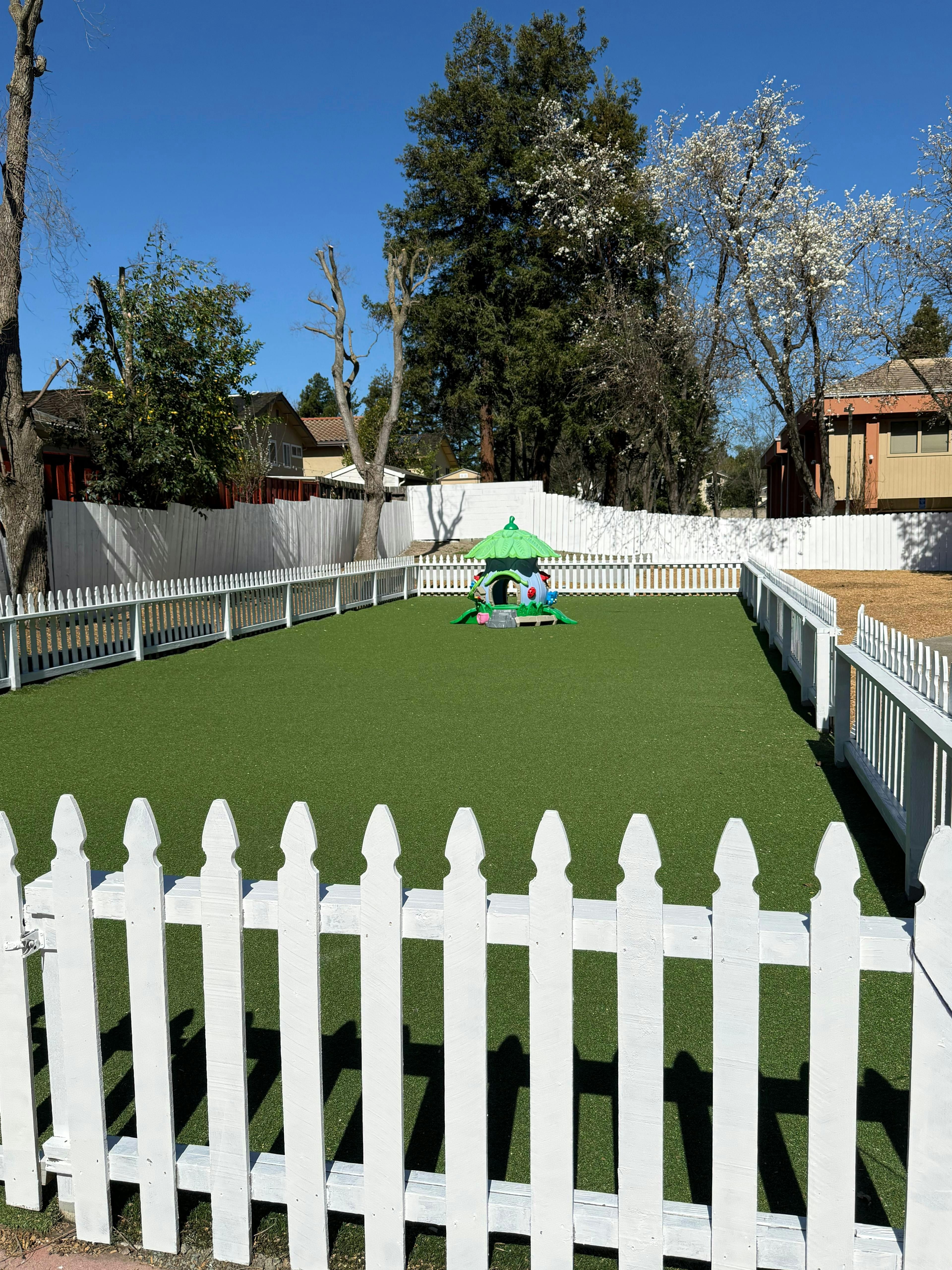 Empty fenced turf play area with a small playhouse