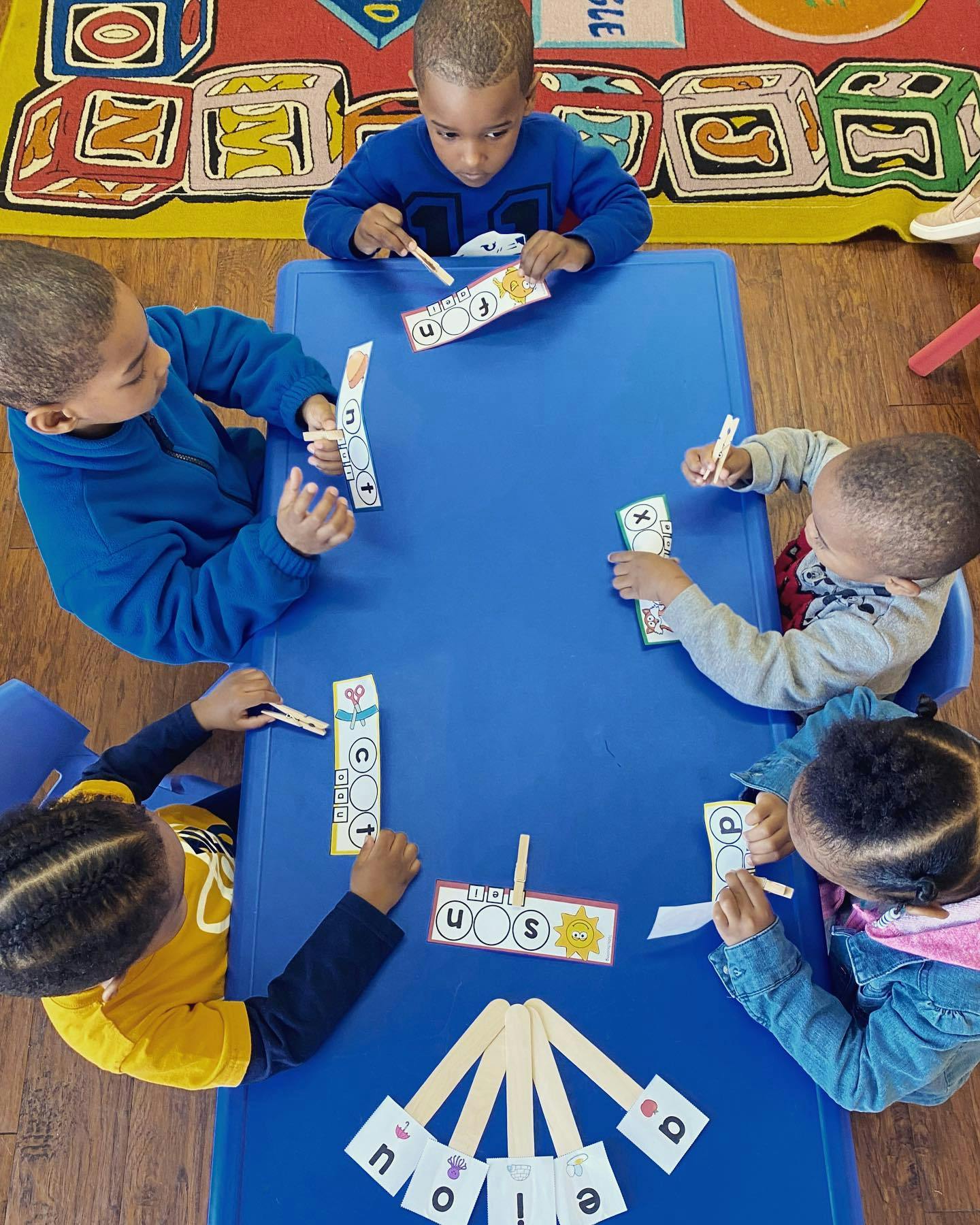 Children at a blue table playing with letter cards and clothespins