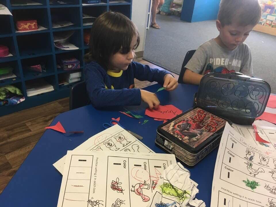 Two children at a table with papers and craft supplies
