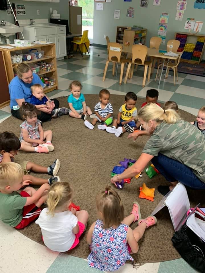 Adults and children sitting in a circle on the floor playing with toys