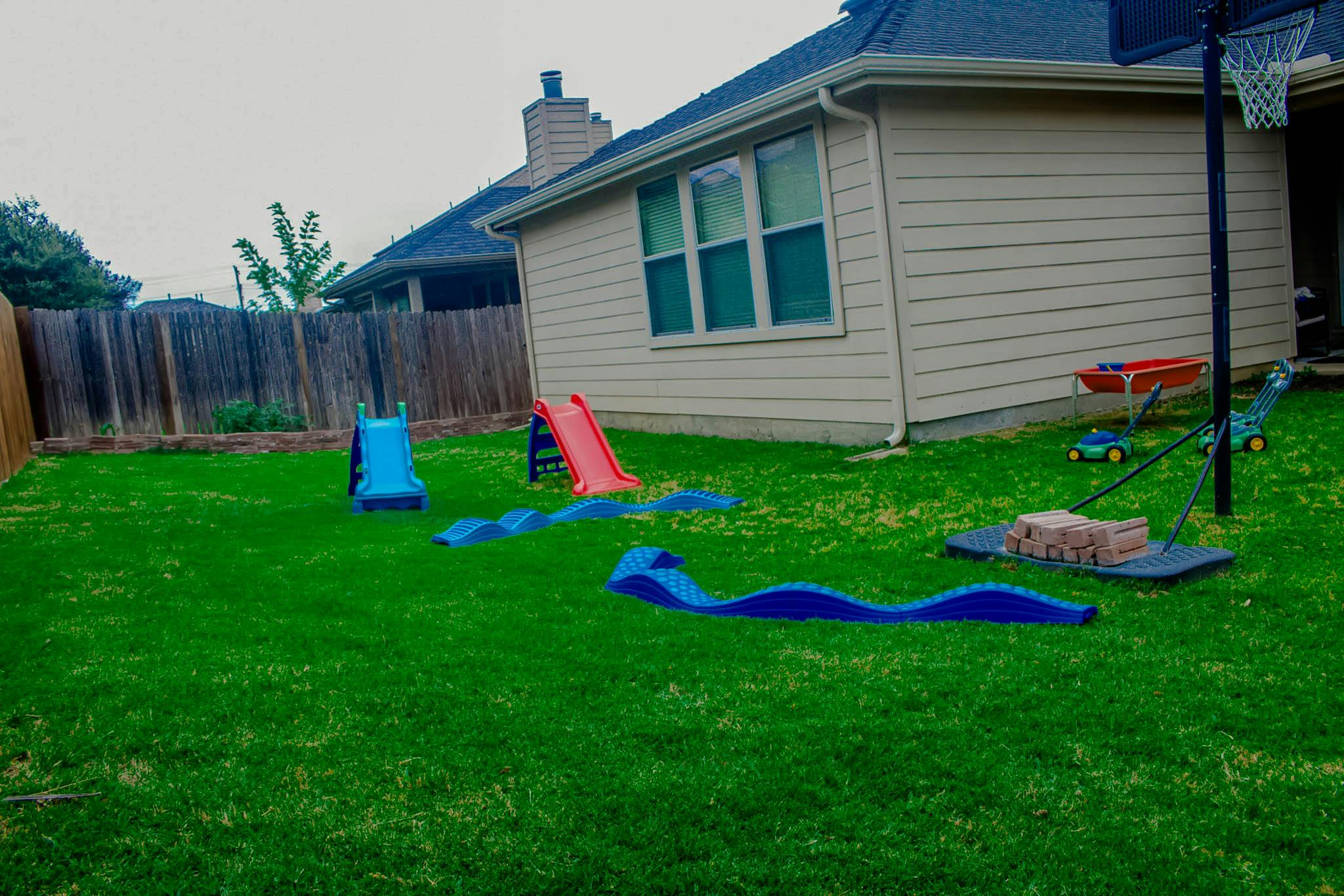 Backyard with a blue slide, red slide, and blue plastic play tunnels