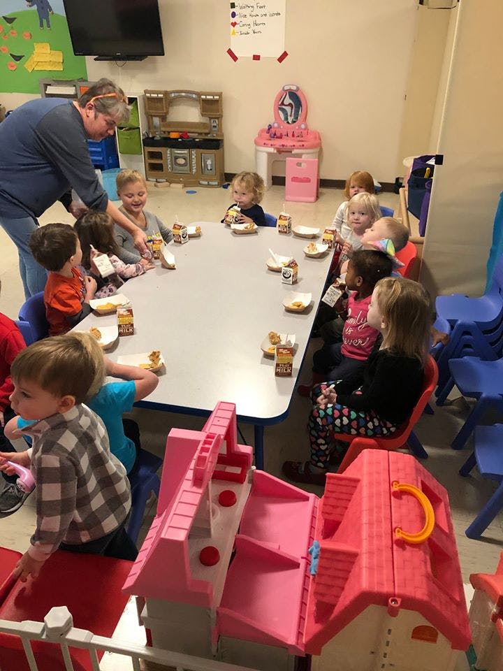 Adult serving snacks to children seated at a table in a classroom