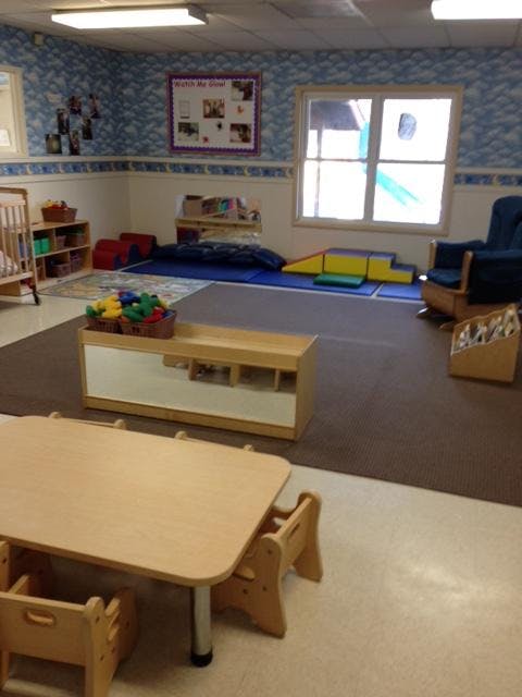 A classroom with small tables and chairs, a crib, and soft play equipment