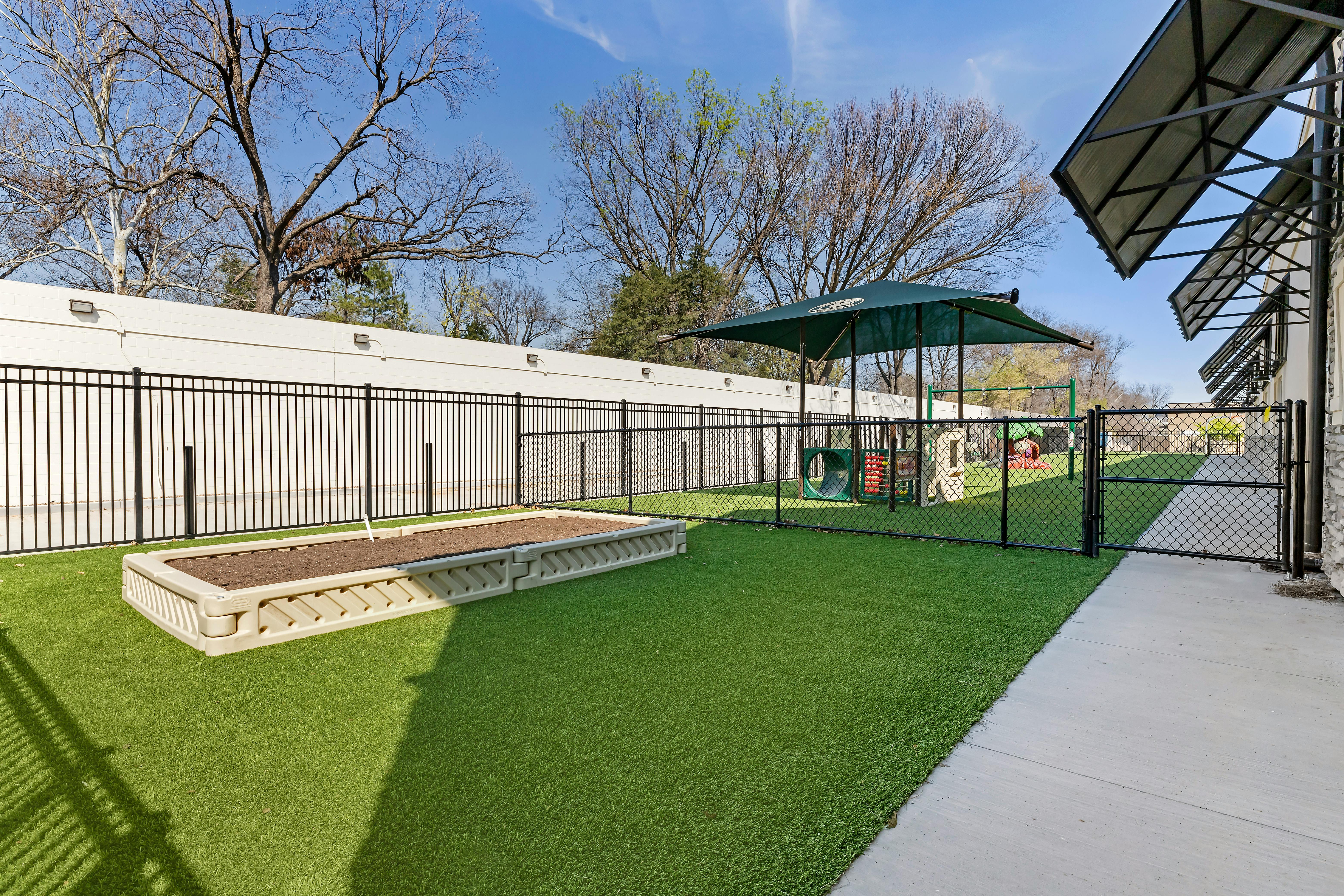 An outdoor playground with artificial turf, a sandpit, and play equipment