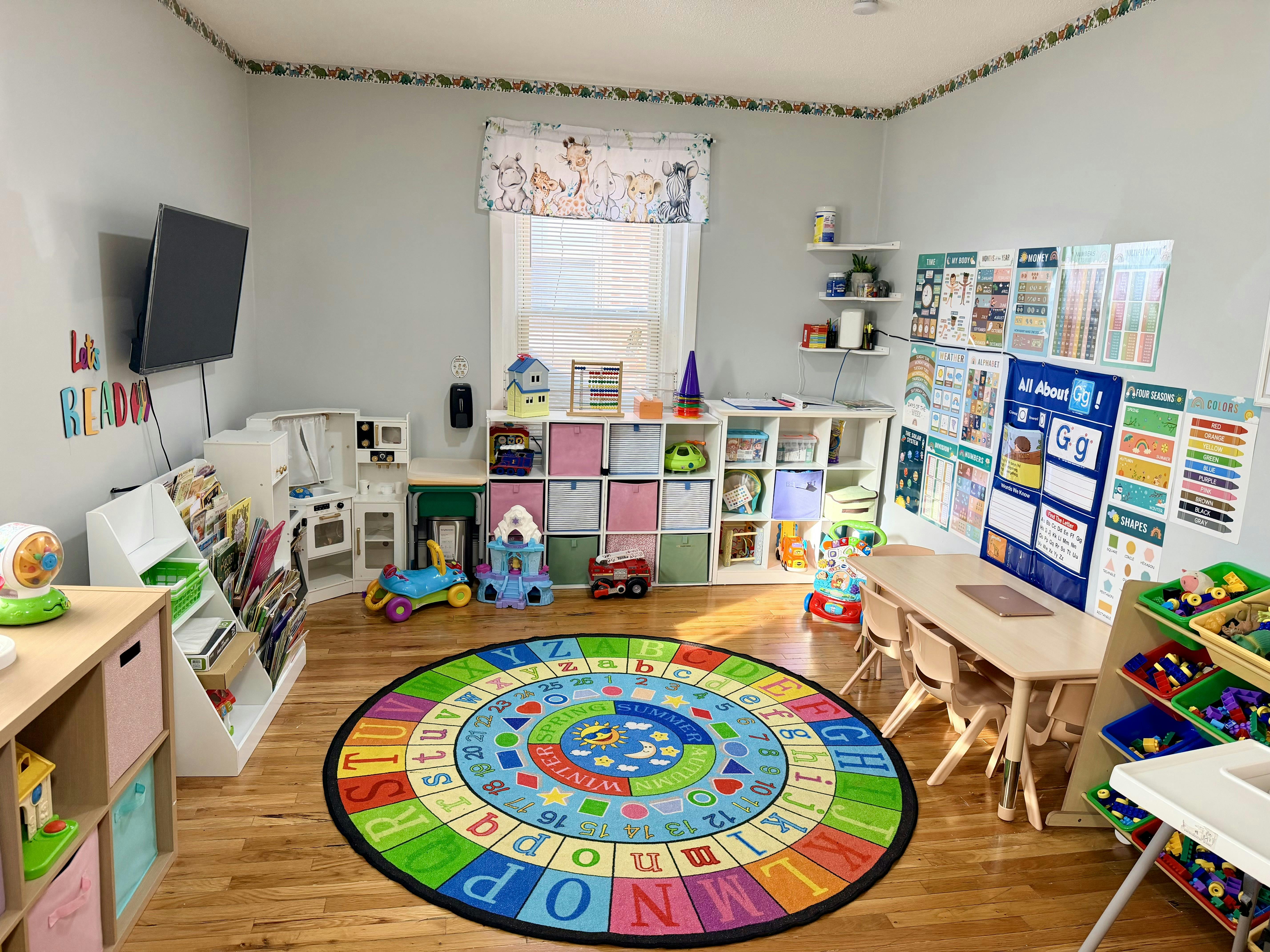 A colorful playroom with a round alphabet rug, small tables, and shelves of toys