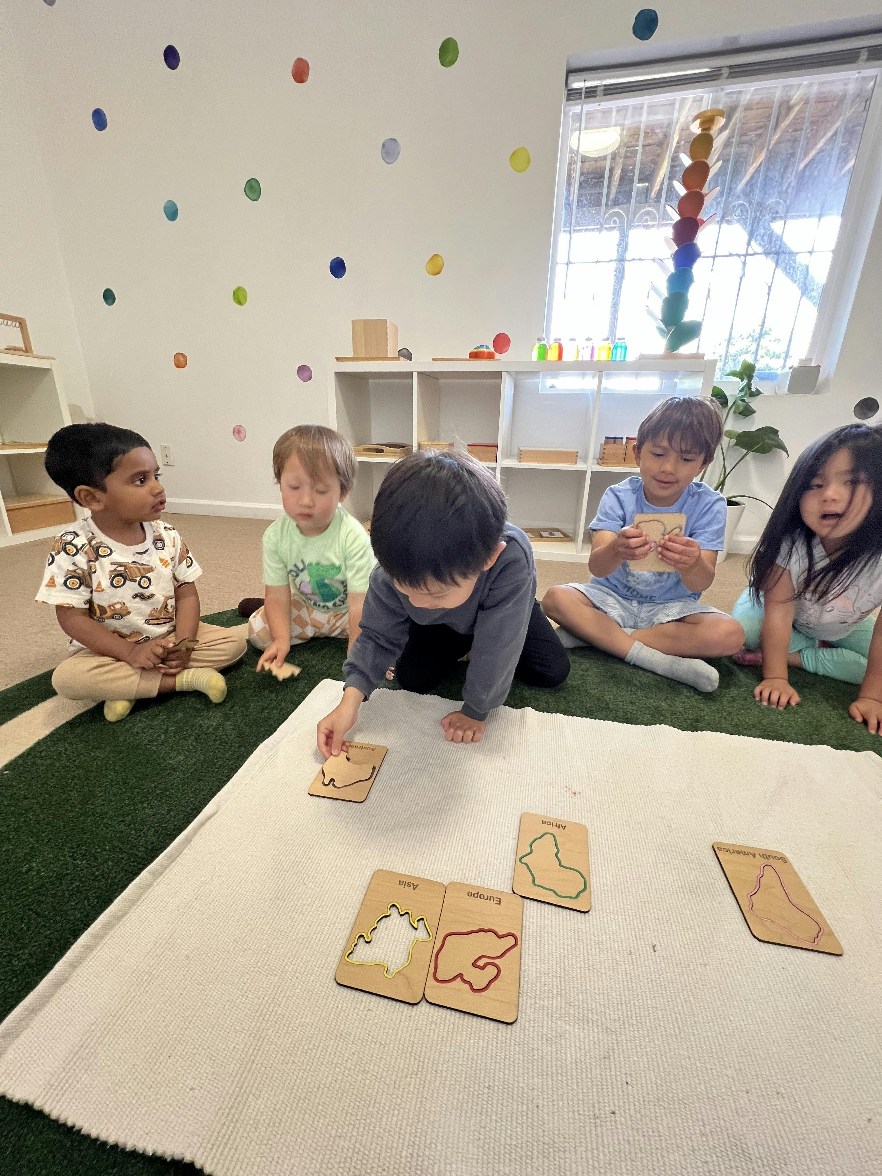 Five children sitting on a rug and playing with geography puzzle boards