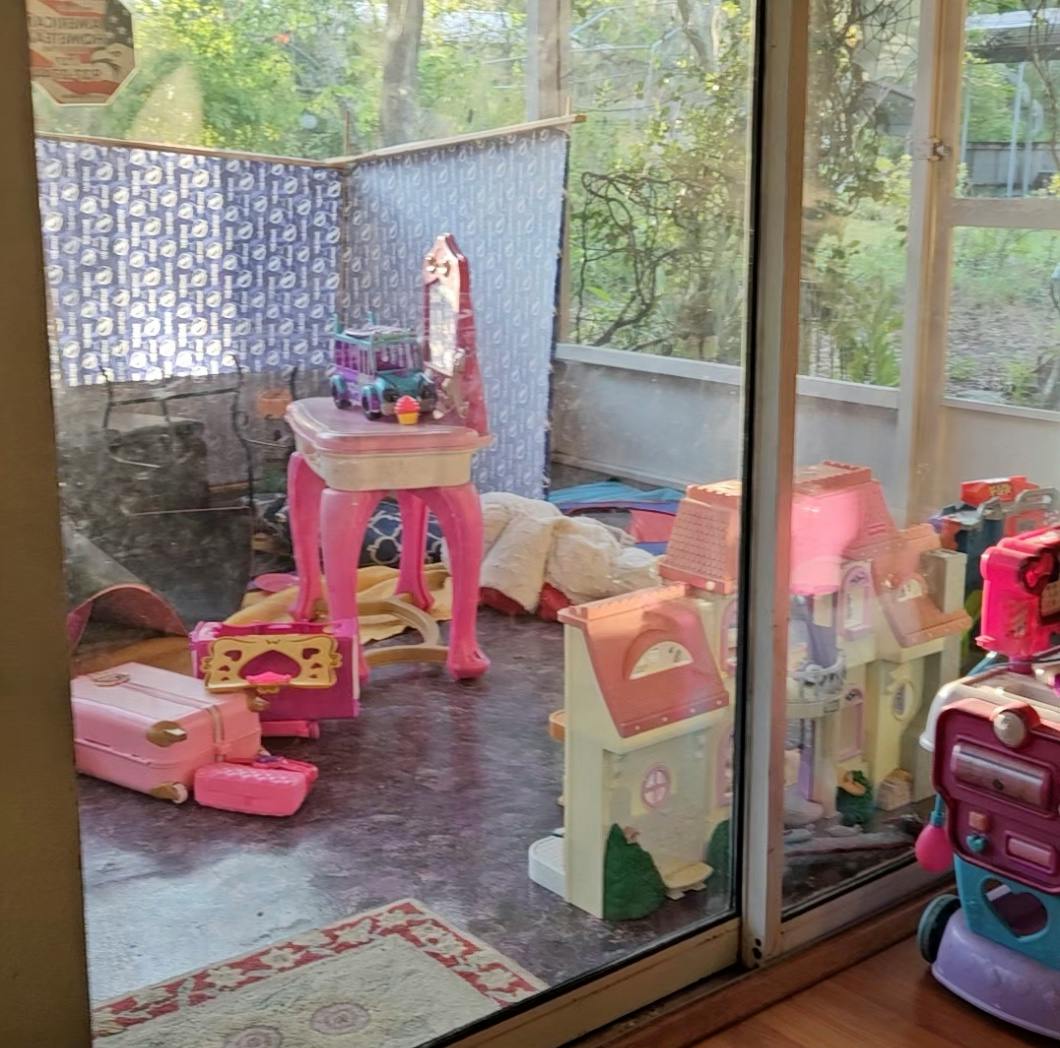 Child's room with a pink vanity, dollhouse, and play luggage