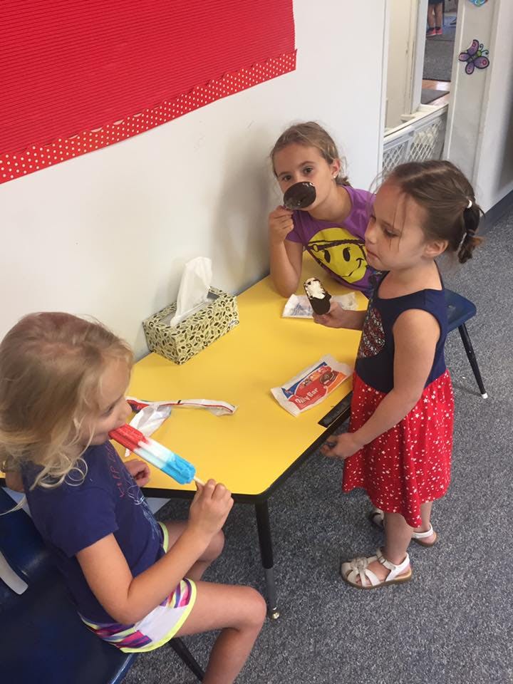 Three children eating frozen treats at a yellow table
