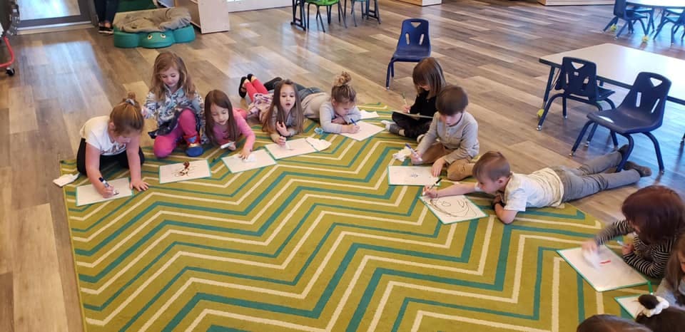 Children lying on a rug and drawing on paper