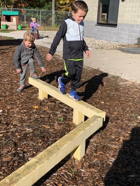 Two children walking on a wooden balance beam outdoors