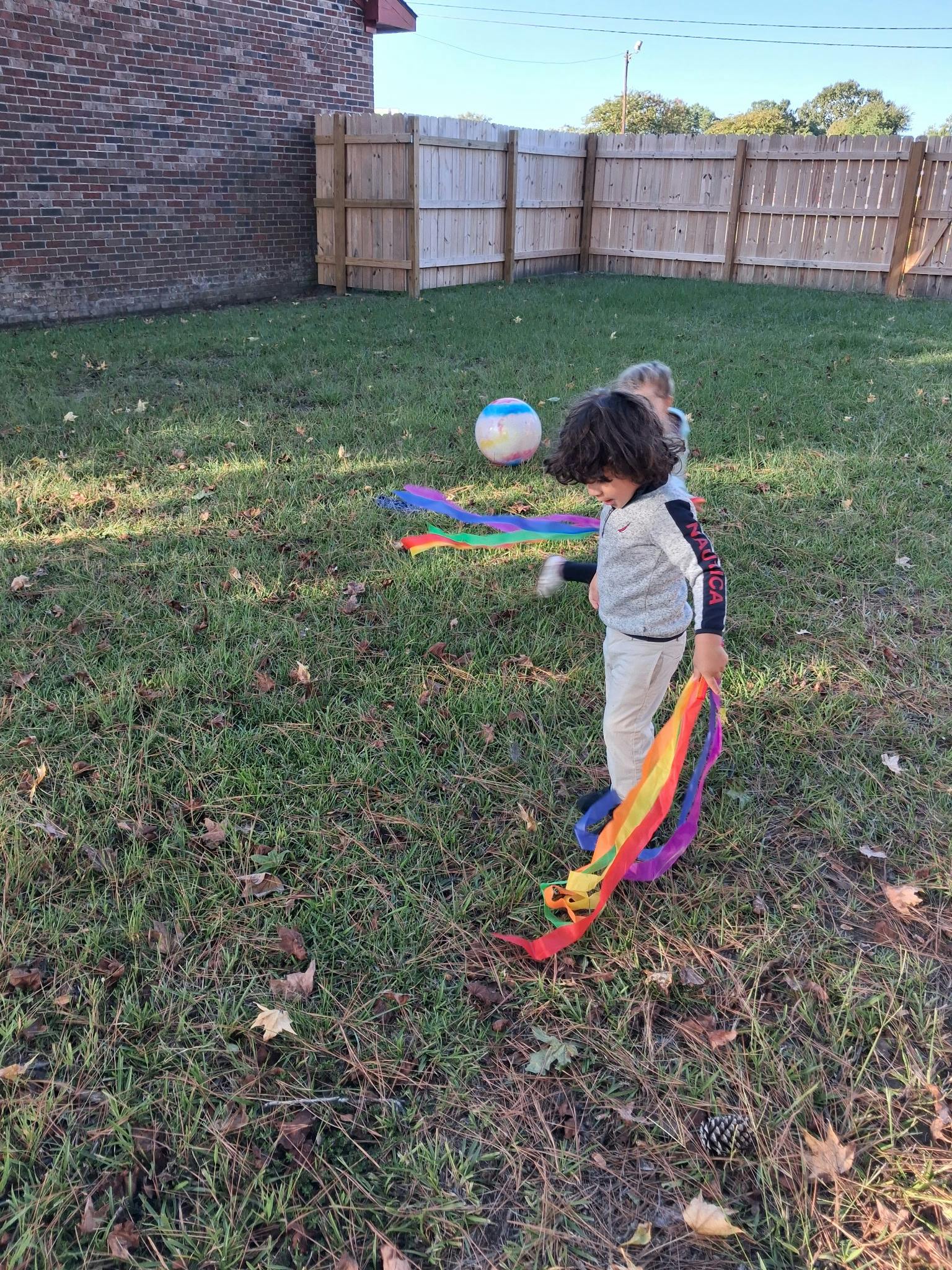 Two children playing with colorful ribbons in a backyard