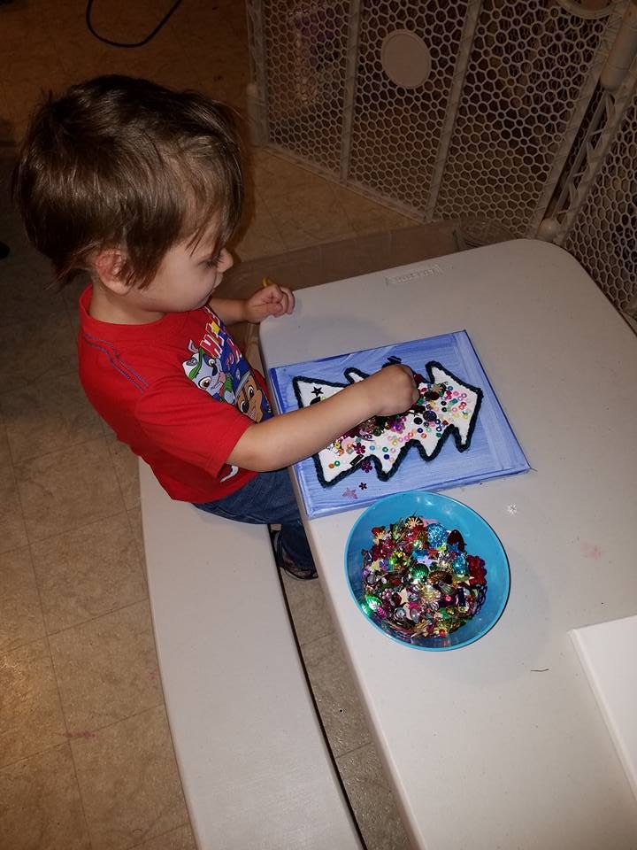 Child decorating a tree-shaped craft with glitter and sequins