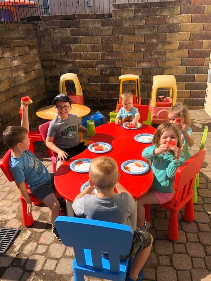 Children eating watermelon at a red table outdoors