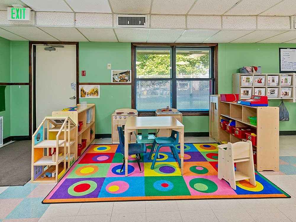 Children's playroom with colorful rug, small tables and chairs, and toy shelves