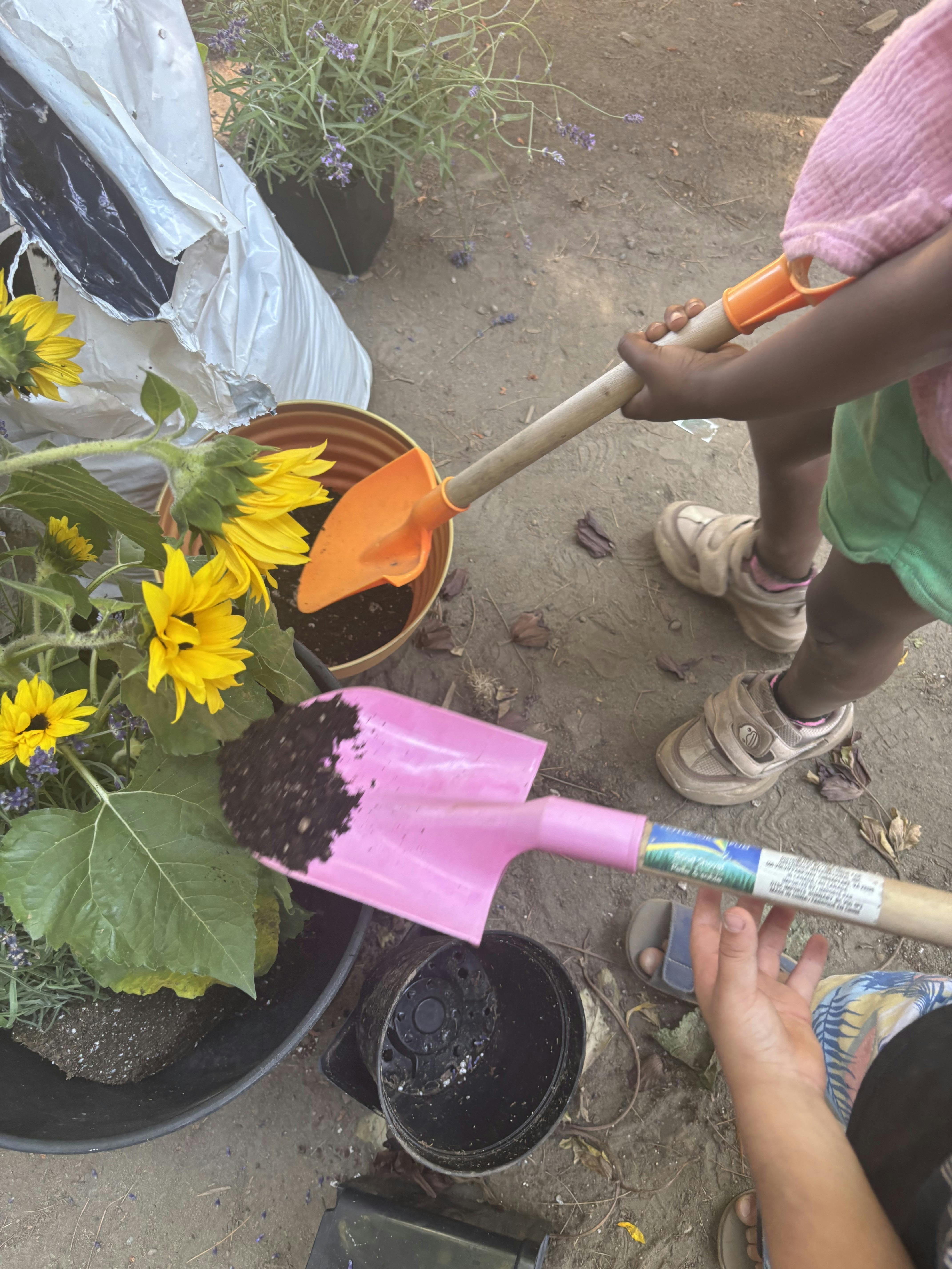 Children using small shovels to scoop soil into plant pots