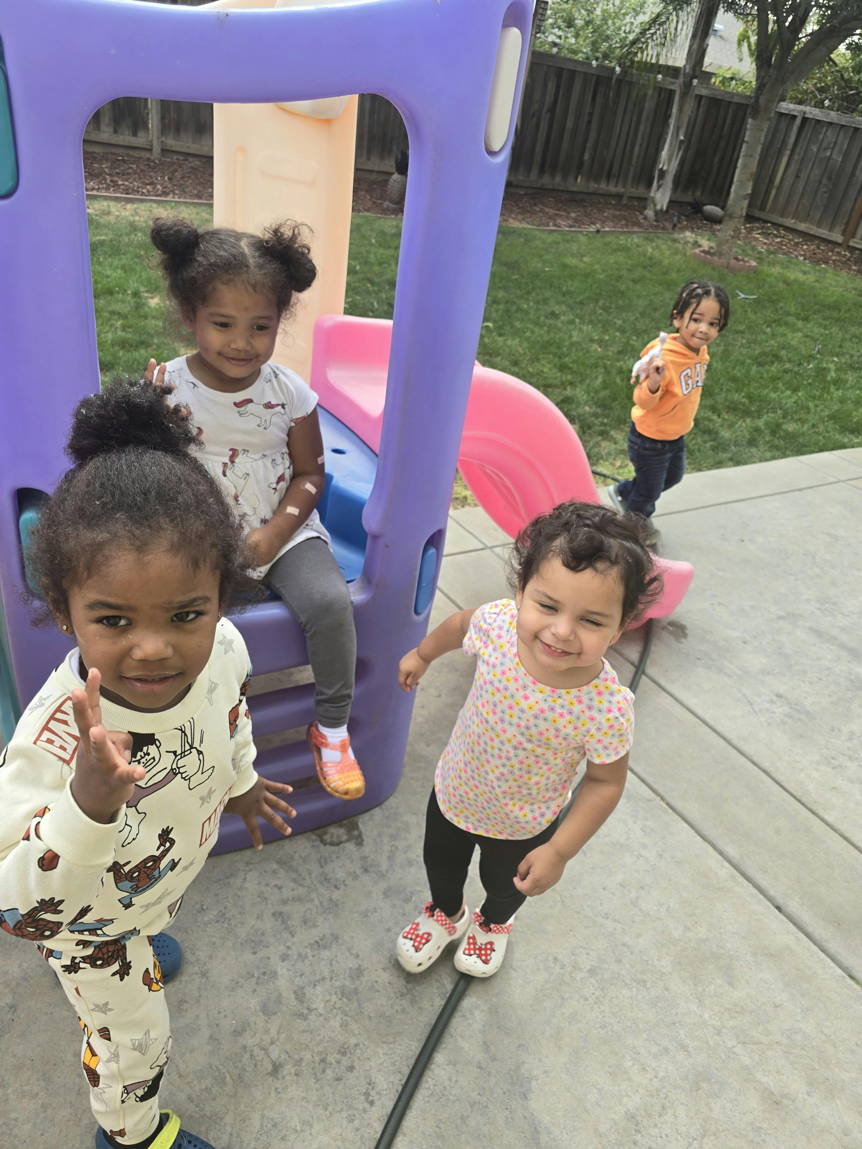 Three children playing on and around a purple and pink playground slide