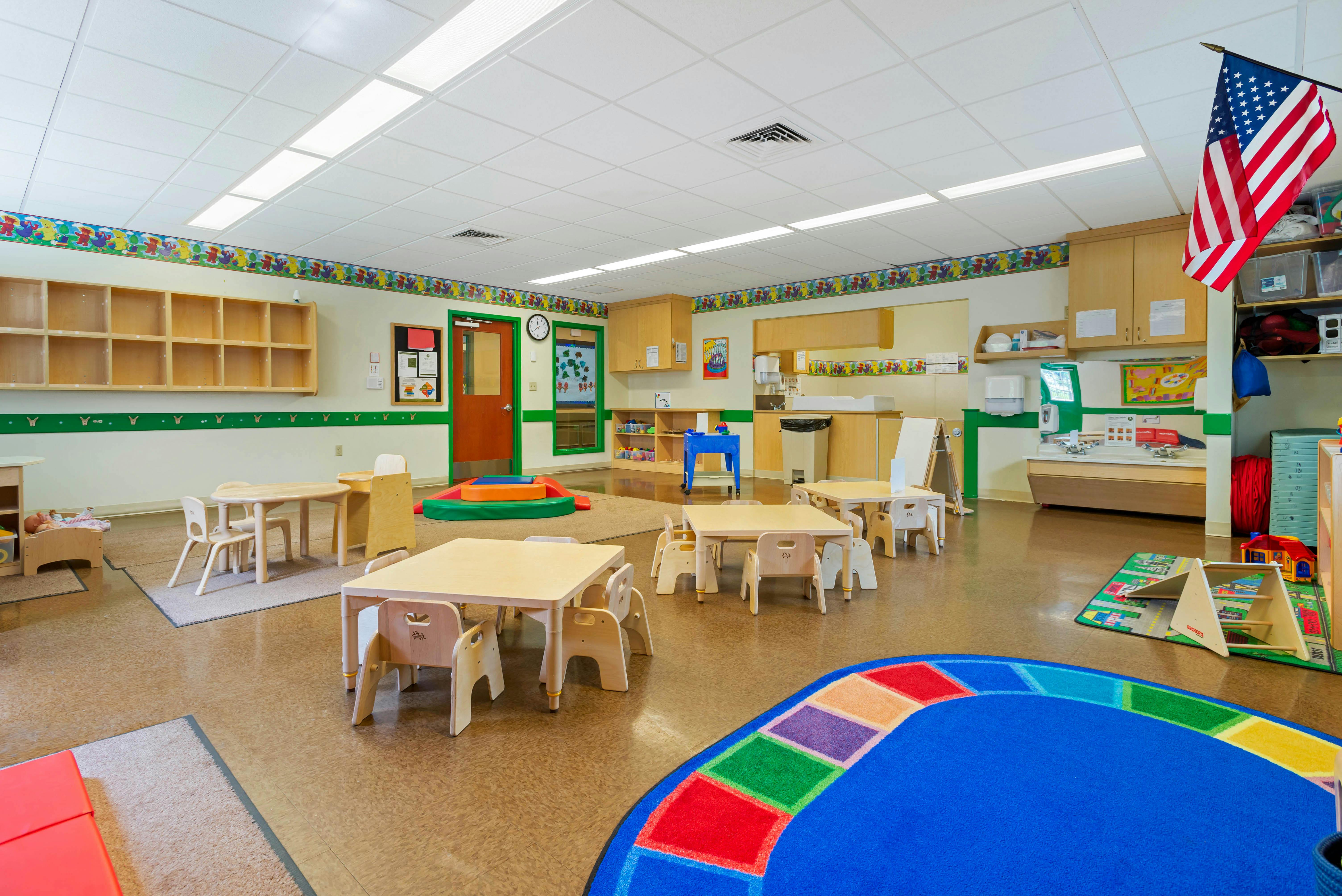 Classroom with small tables and chairs, shelves, and an American flag
