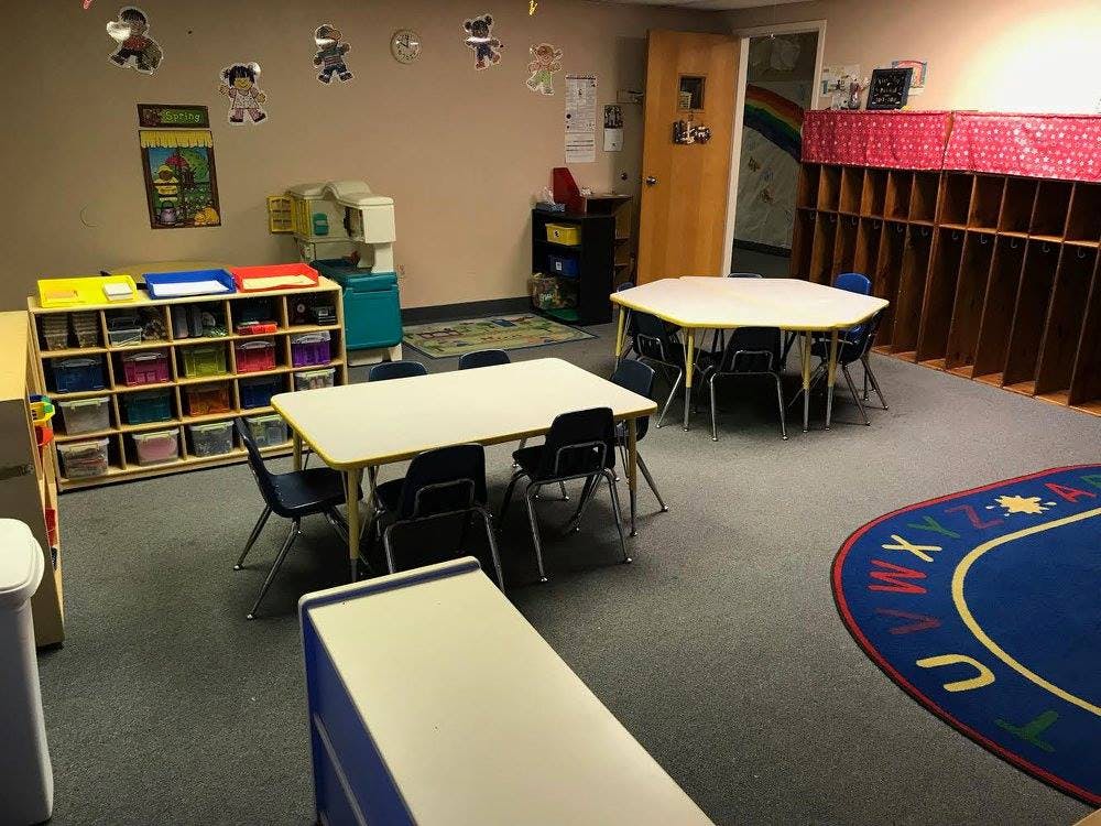 Empty classroom with small tables and chairs, storage cubbies, and a rug