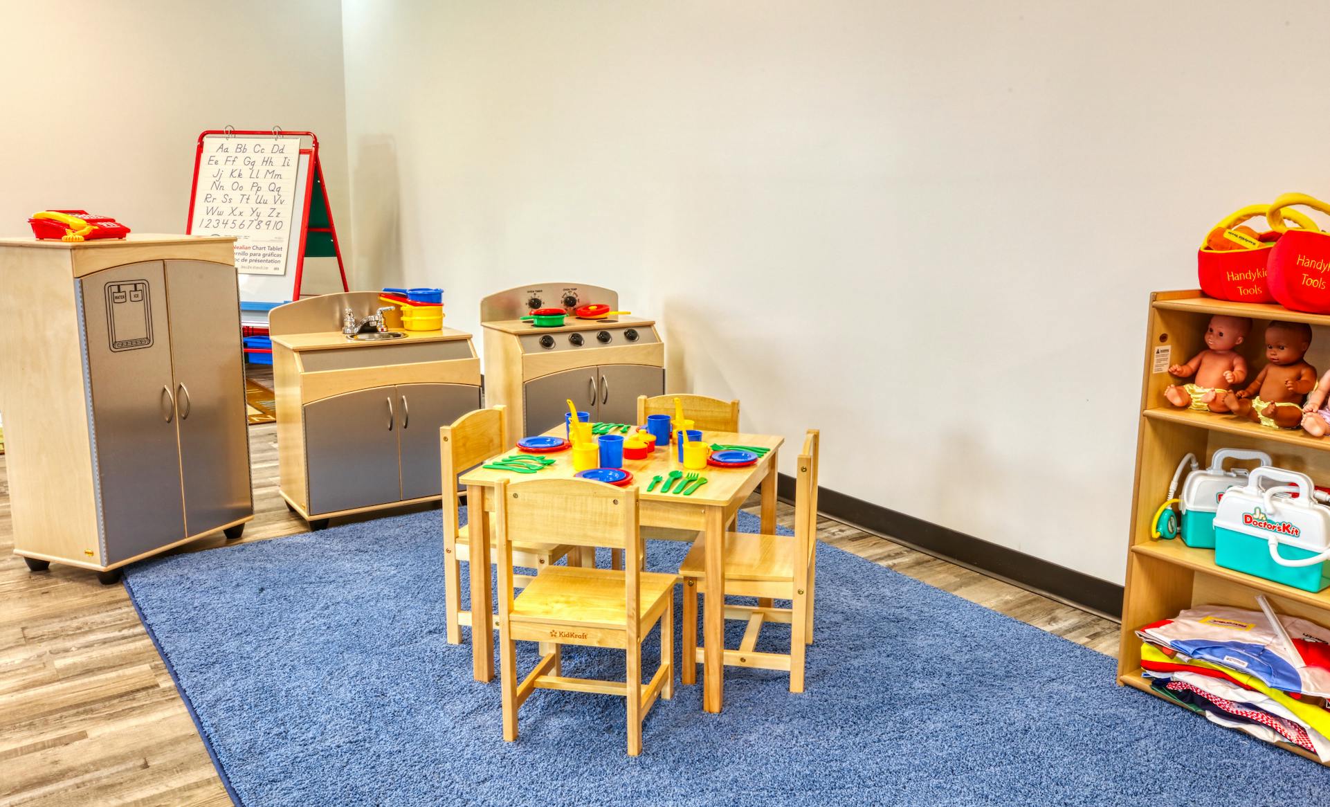playroom with toy kitchen set, table, chairs, and shelves of dolls and dress-up clothes