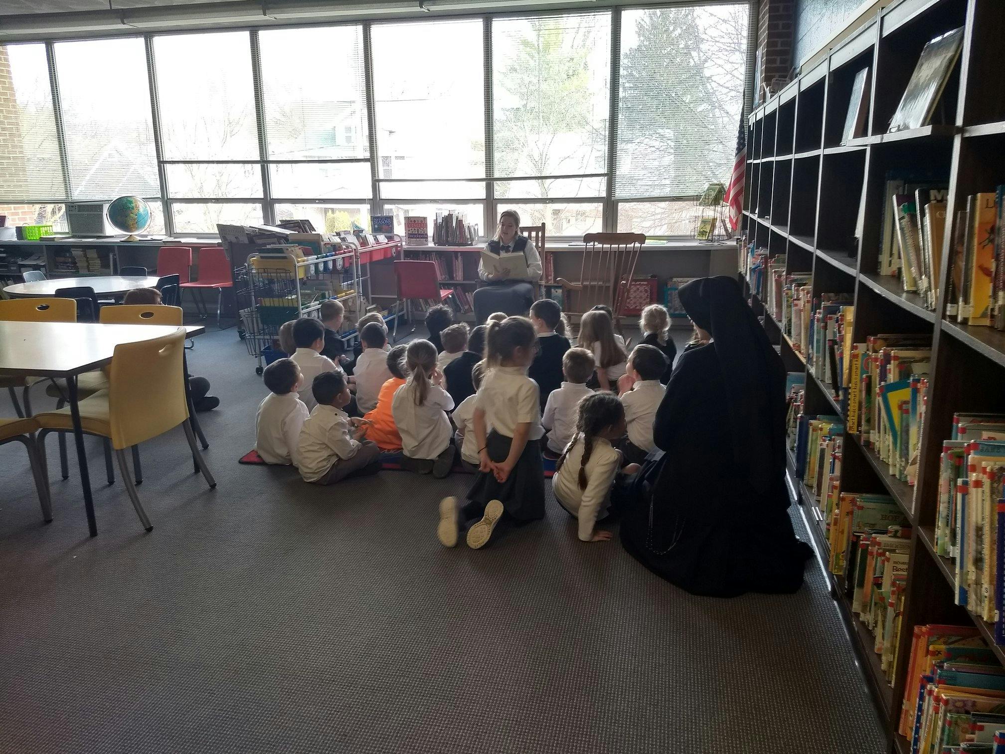 Children sitting on the floor listening to a person reading in a library