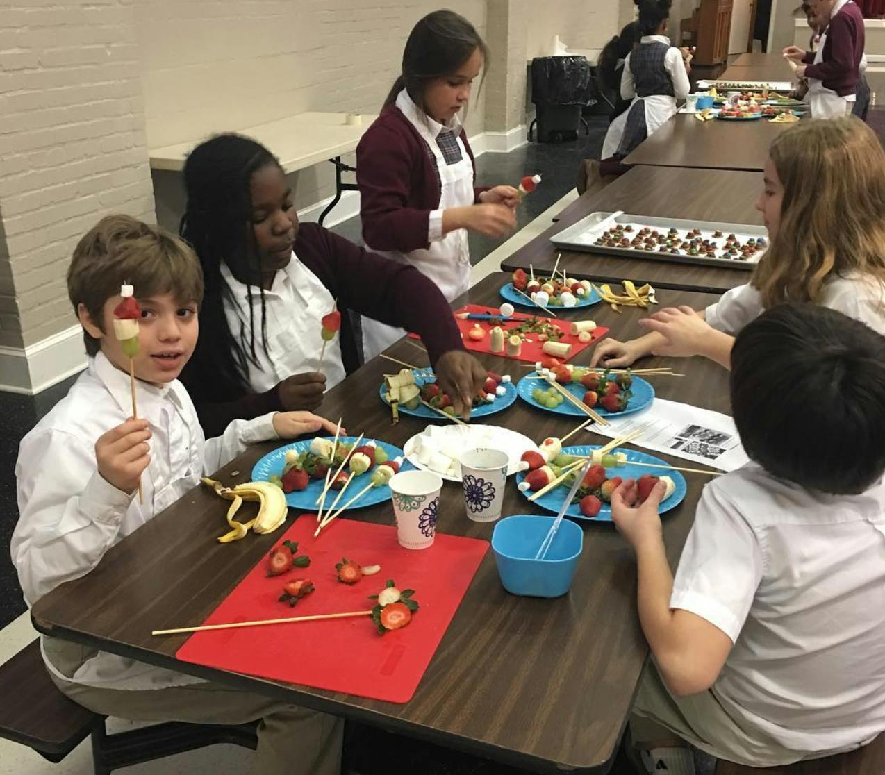 Children making fruit skewers at a table
