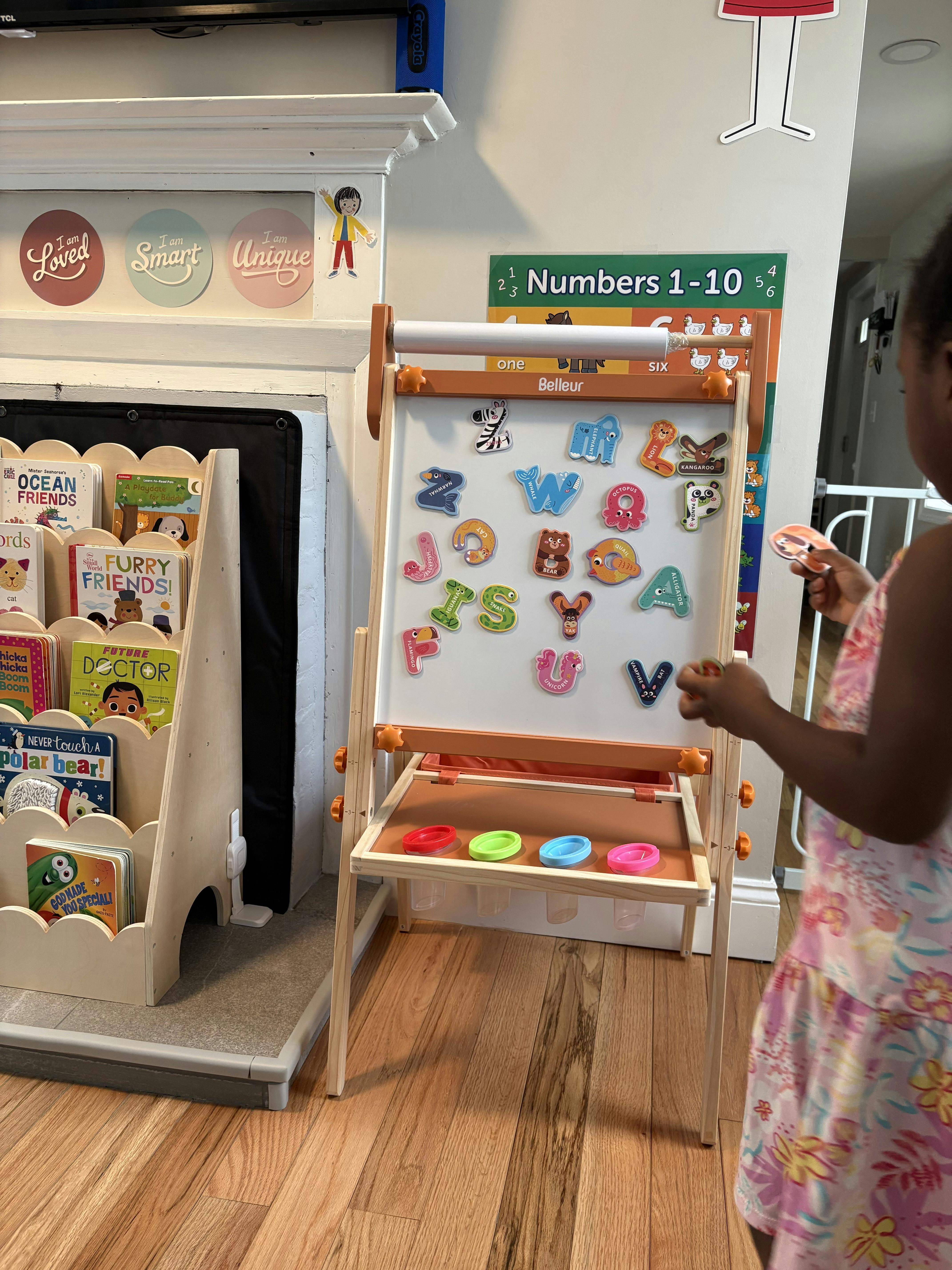 Child placing magnetic letters on a white easel in a playroom