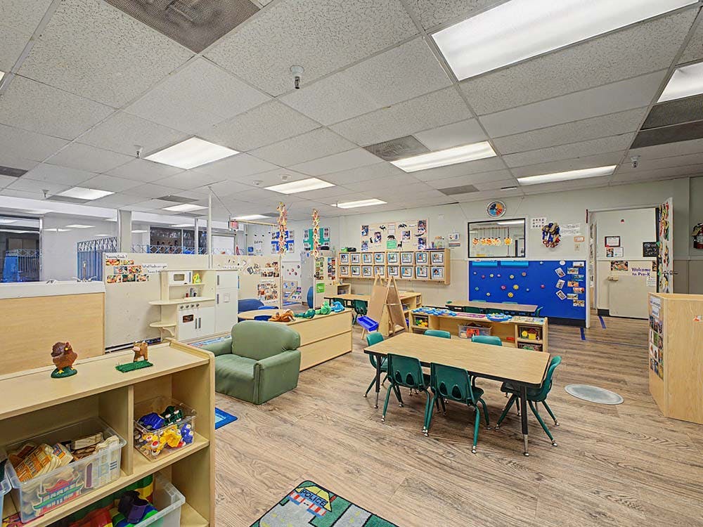 Empty classroom with small tables and chairs, play kitchen, and cubbies