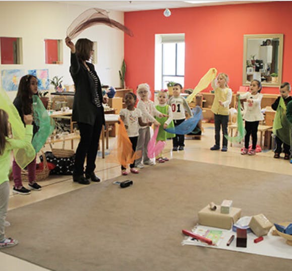 Person and children holding colorful scarves in a classroom