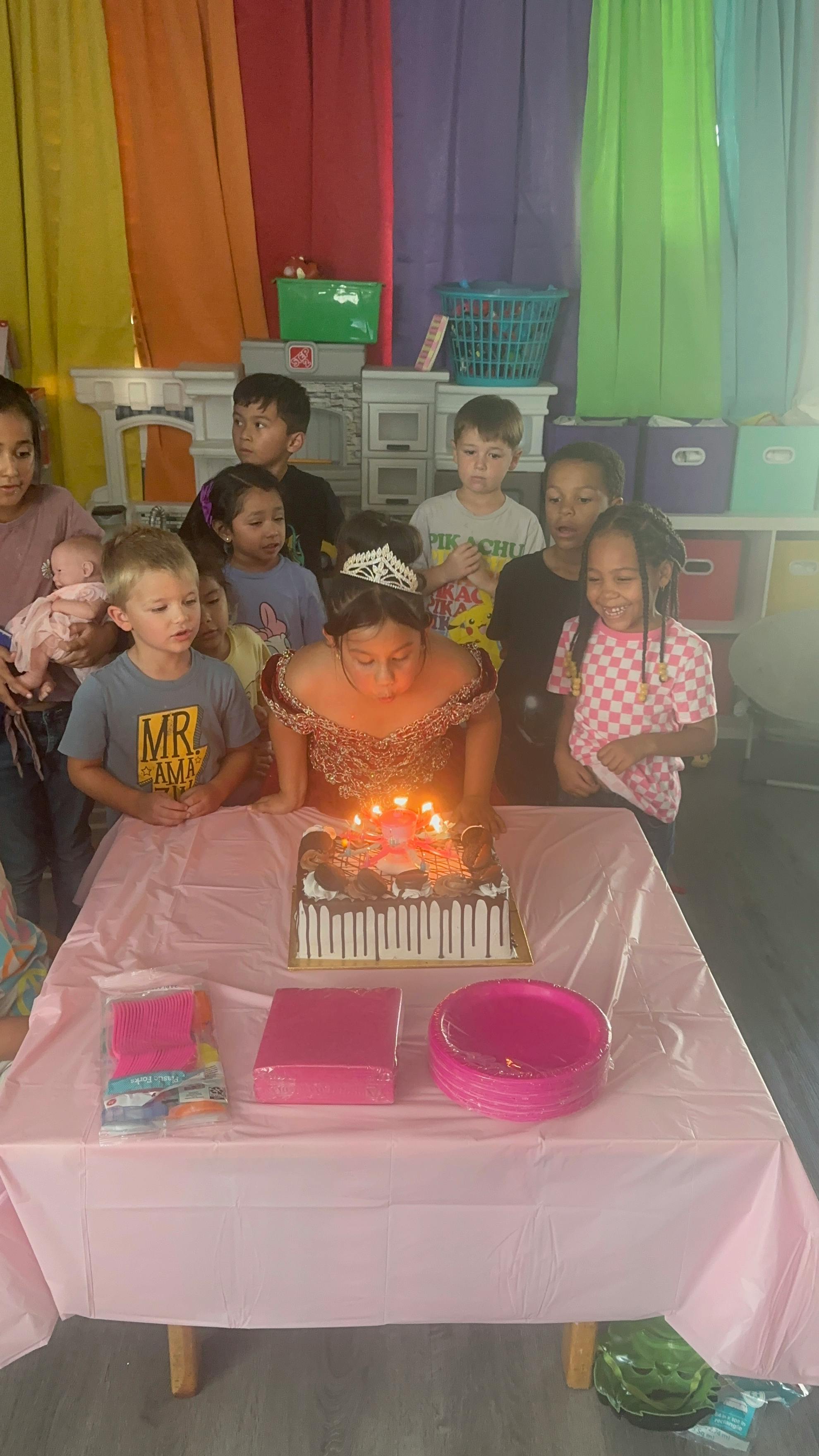 Child blowing out candles on a birthday cake surrounded by other children