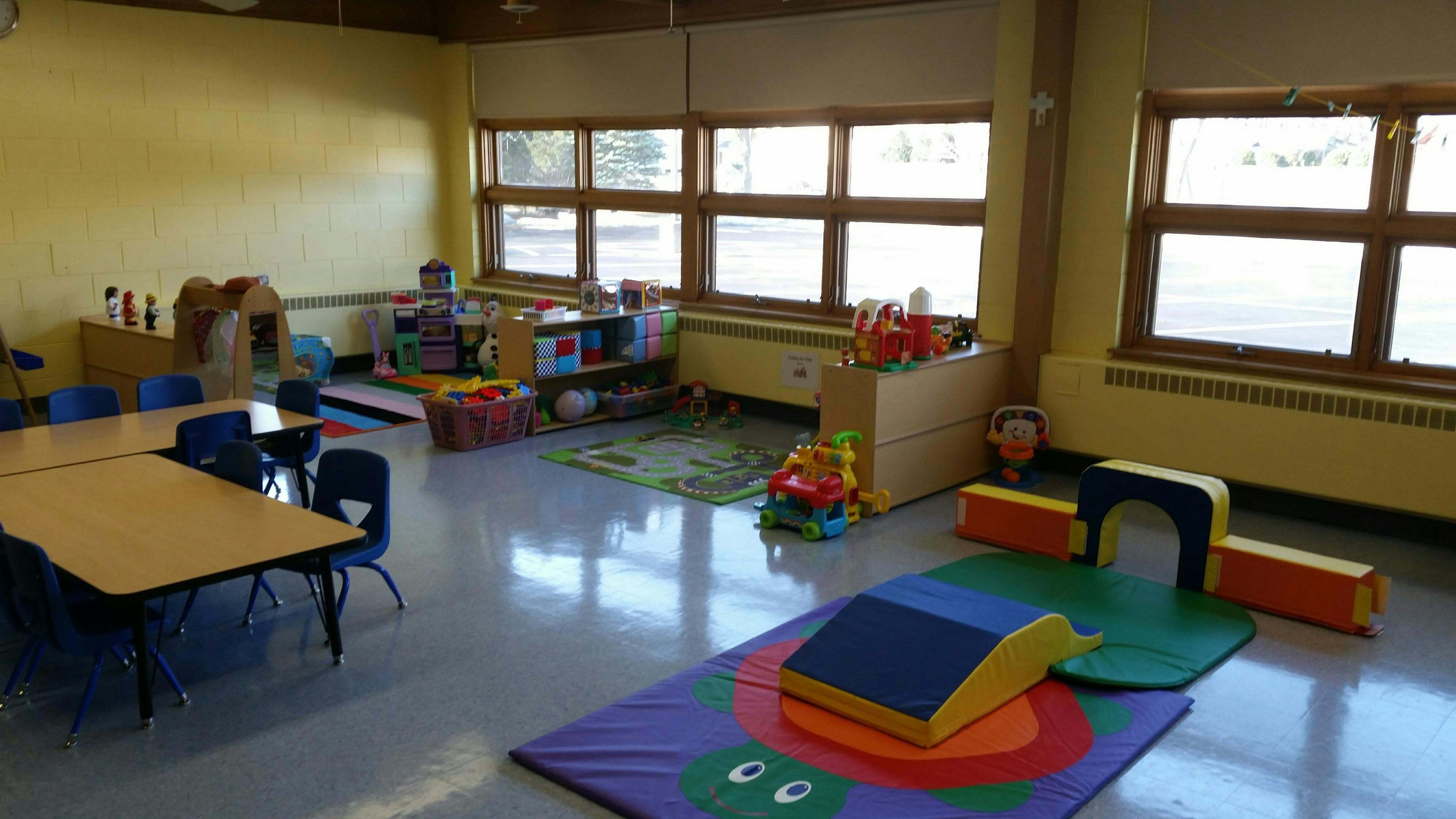 Empty classroom with small tables, chairs, and play equipment