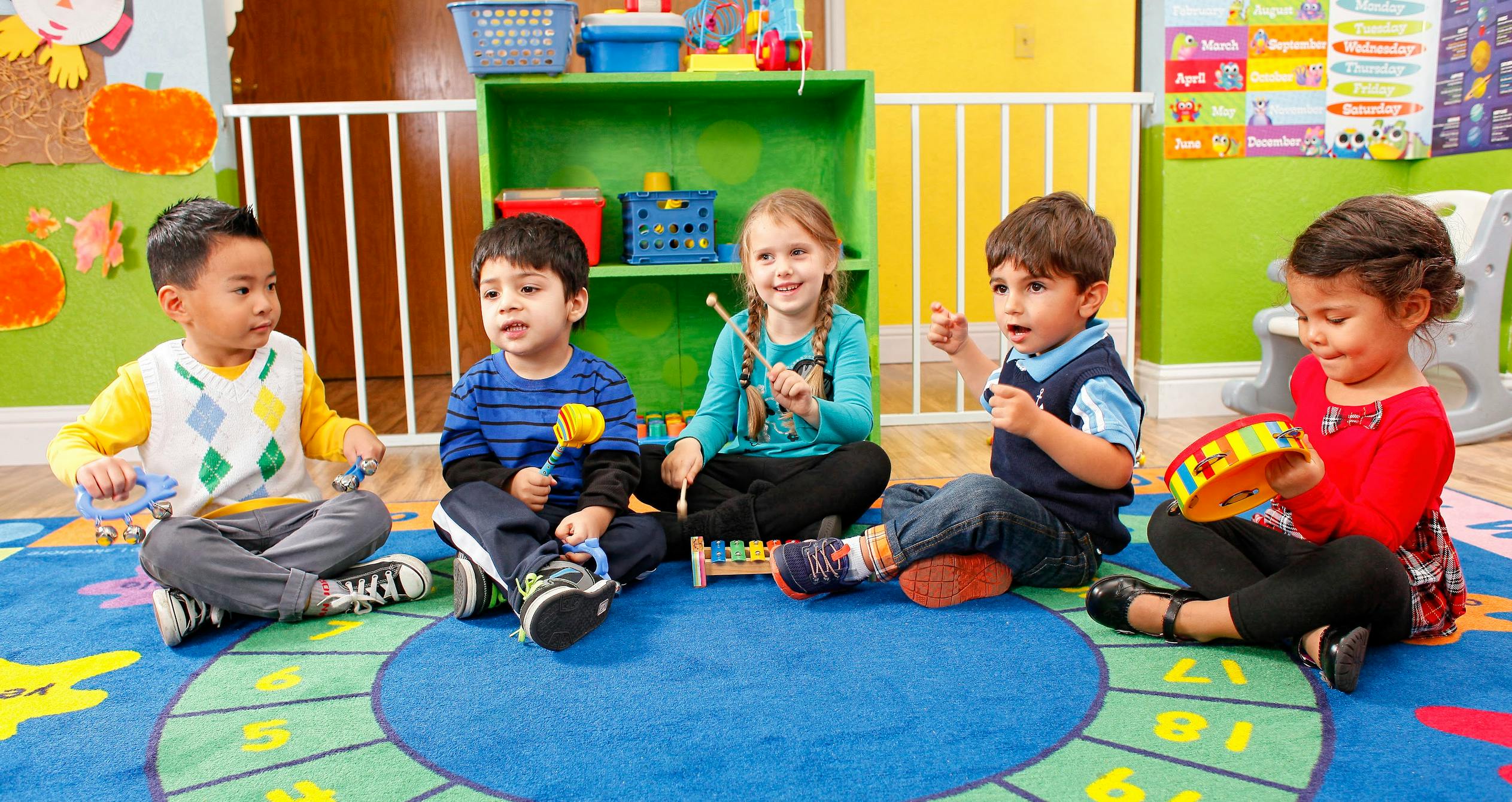Five children sitting on a rug playing musical instruments in a classroom