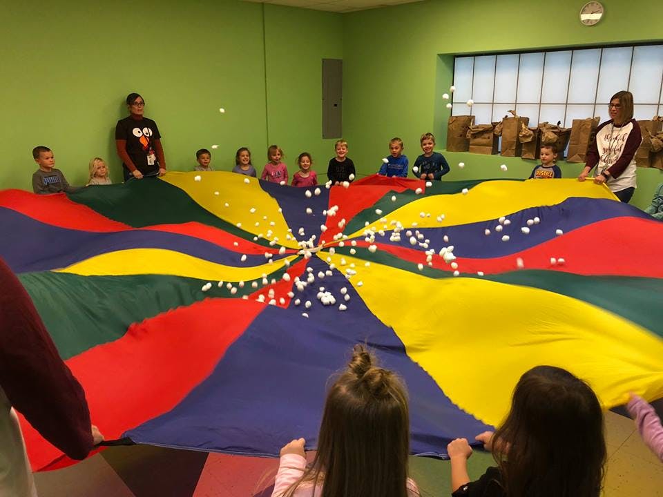 People and children playing with a colorful parachute and small white balls