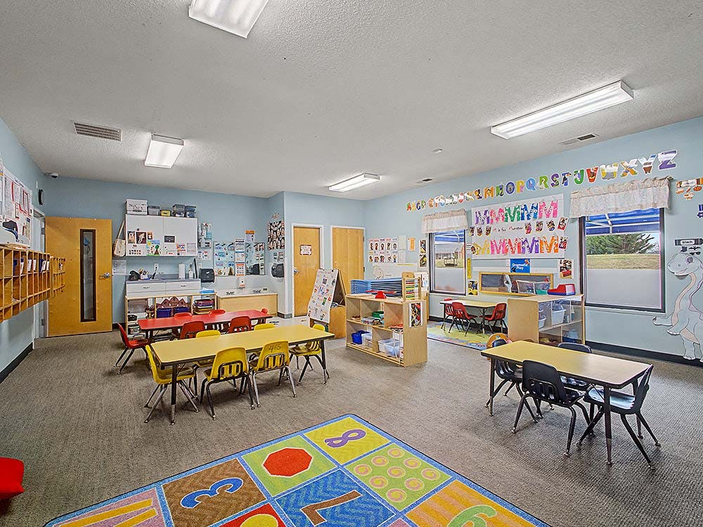 A classroom with small tables and chairs, a colorful rug, and alphabet decorations
