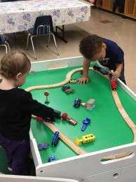 Two children playing with toy trains on a green table