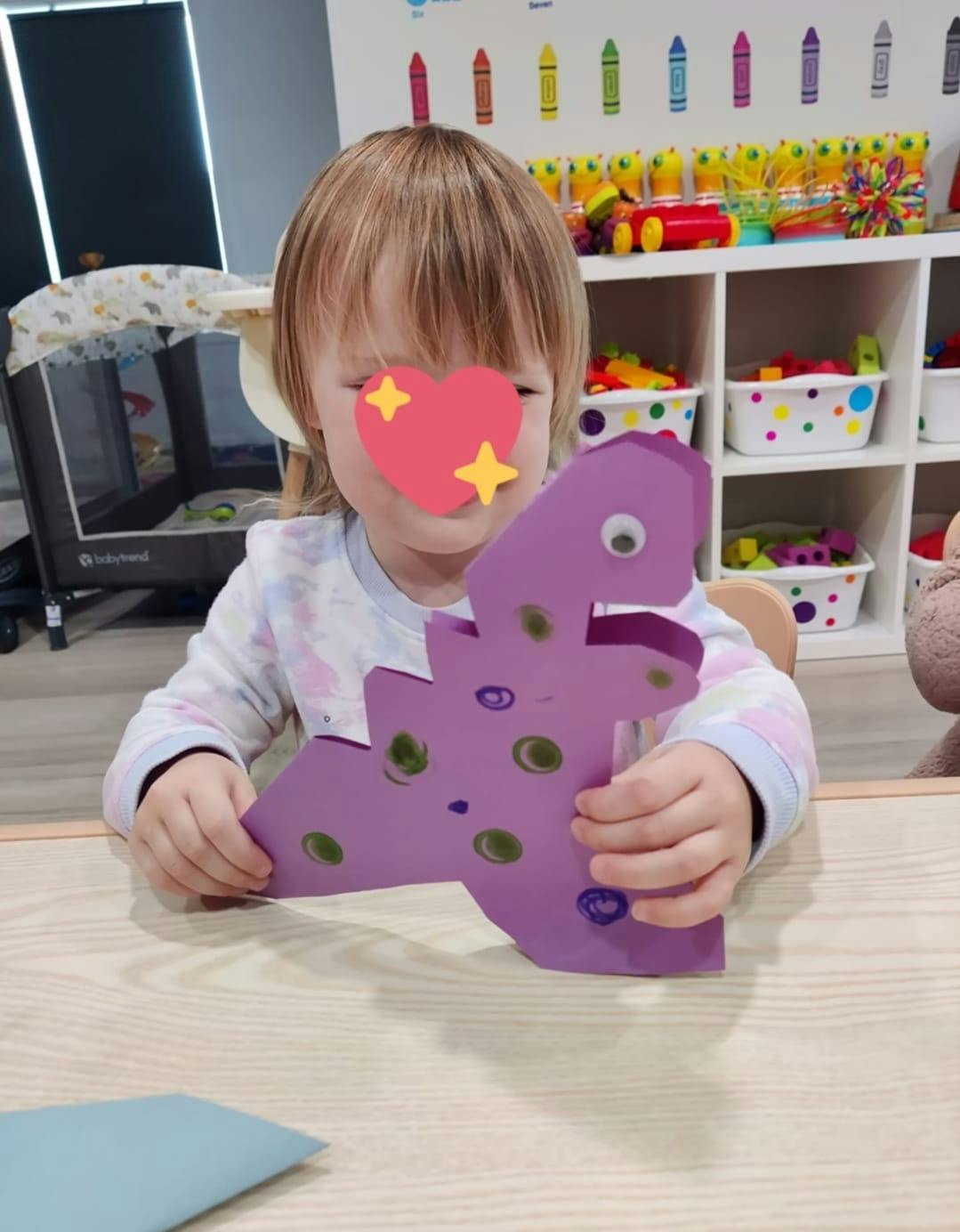 Child holding a purple paper dinosaur craft at a table