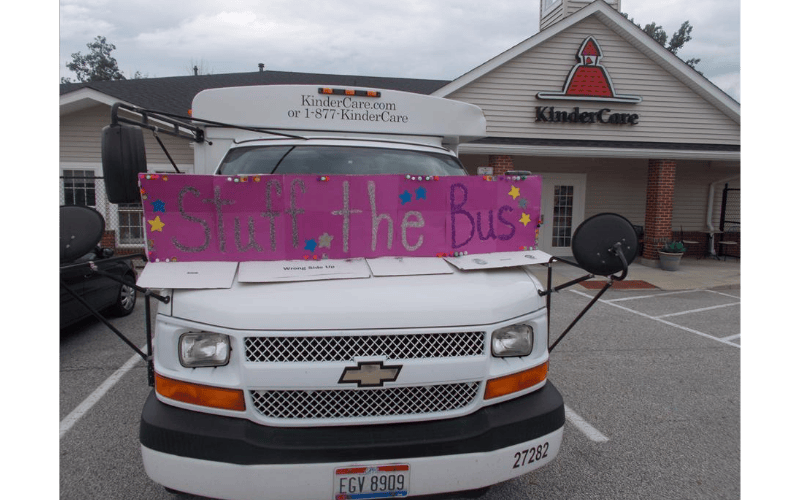 White KinderCare bus with a pink sign on the front that says "Stuff the Bus"