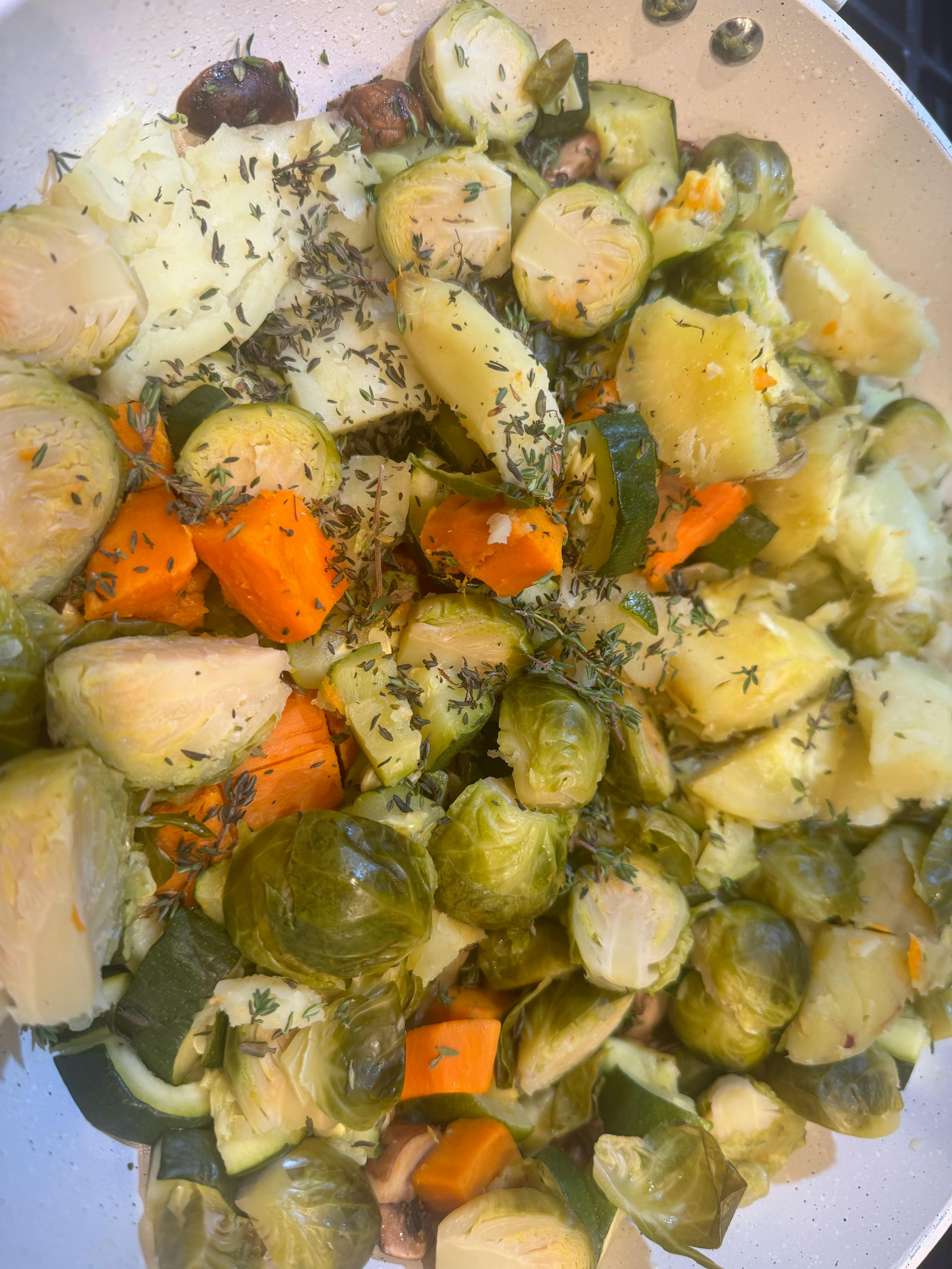 Cooked vegetables including potatoes, carrots, and Brussels sprouts with herbs