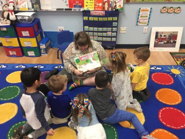 Adult reading a book to a group of children in a classroom