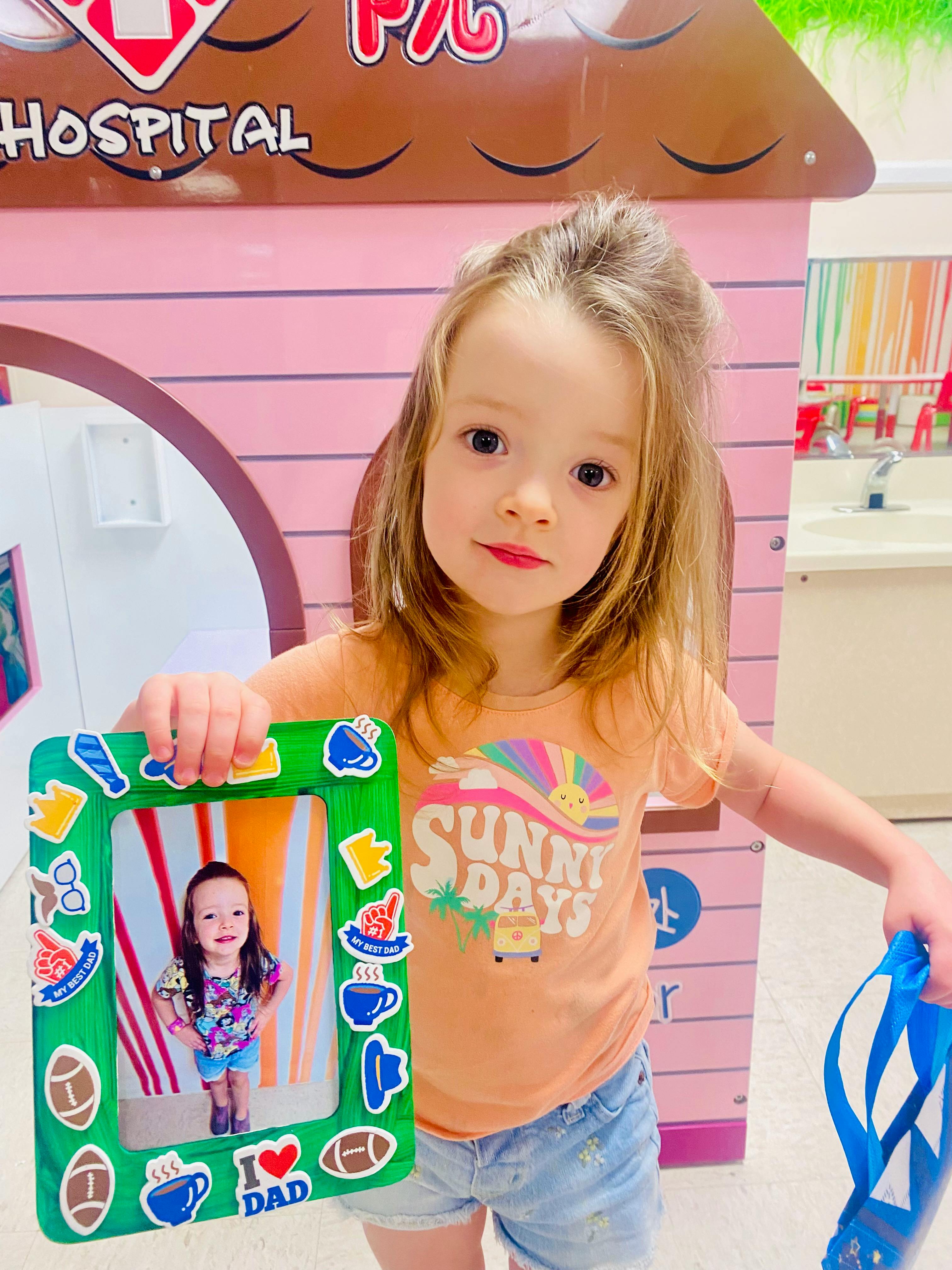 Child holding a green picture frame with a photo of another child