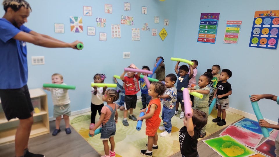 Adult and children in a classroom holding colorful foam noodles