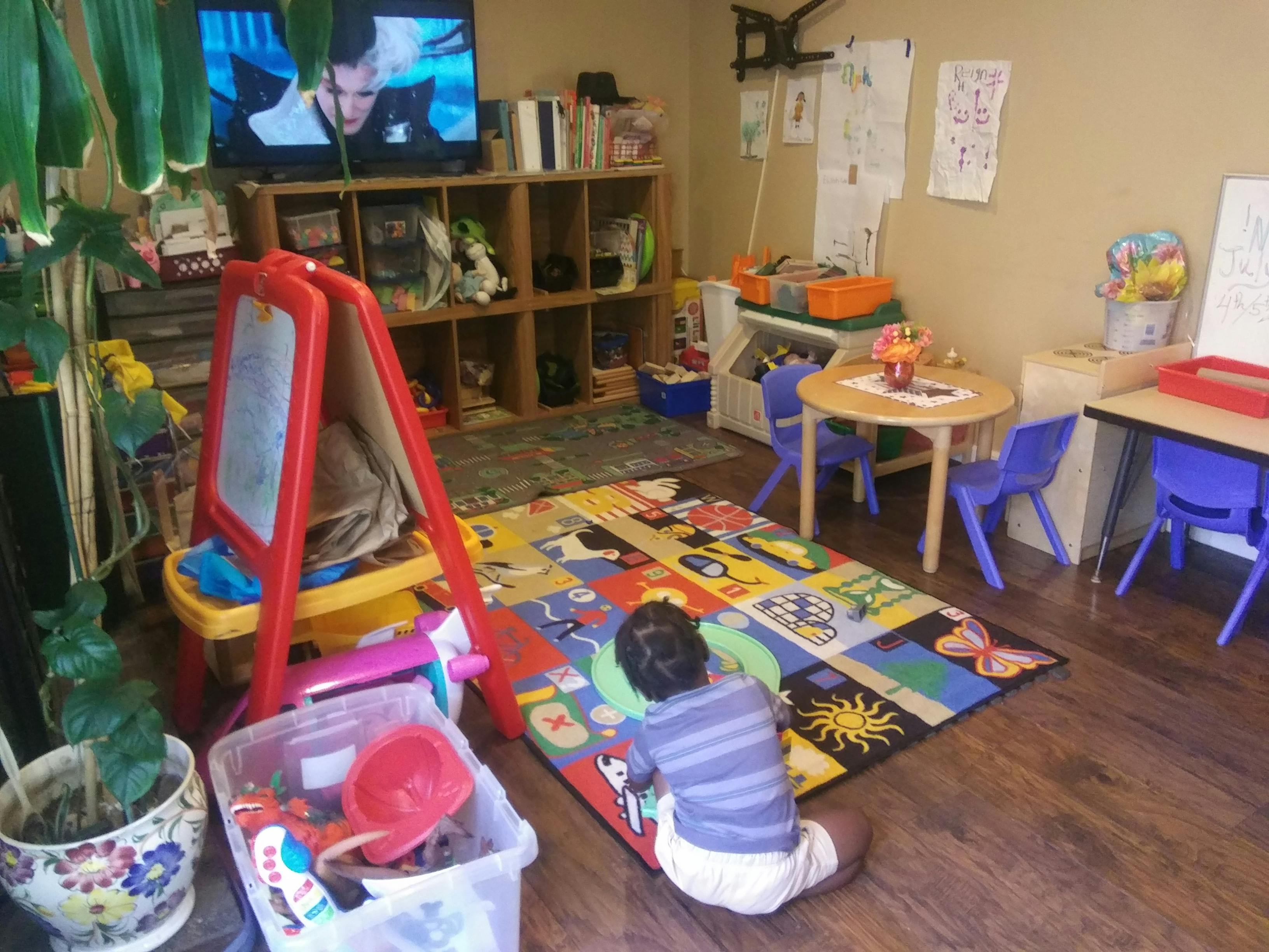 Child on a colorful rug in a playroom with an easel and small tables