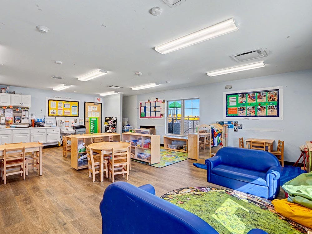 An empty childcare classroom with small tables, chairs, and play areas
