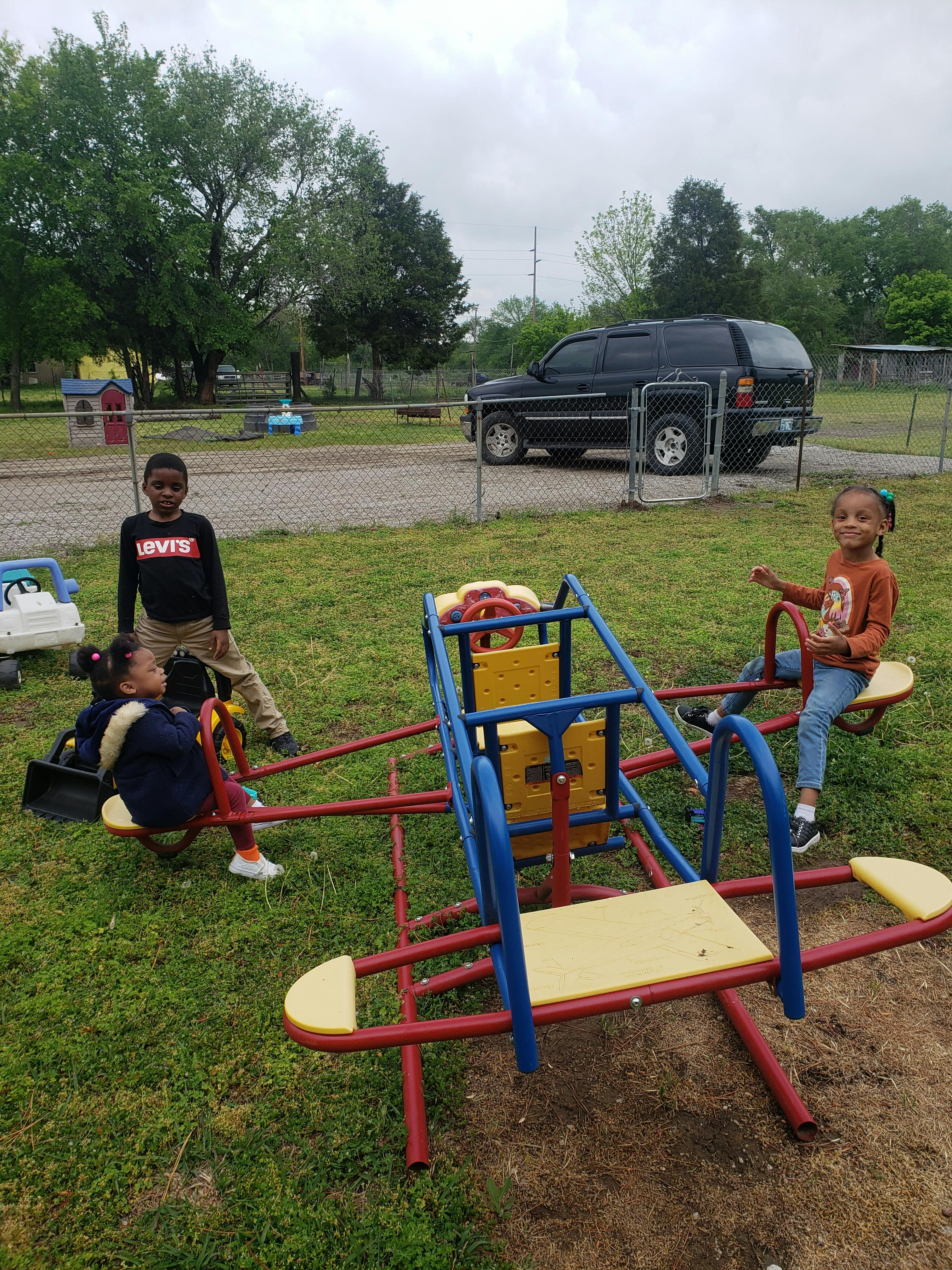 Three children on a playground with a seesaw and merry-go-round