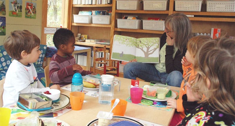 Adult reading a book to children at a table