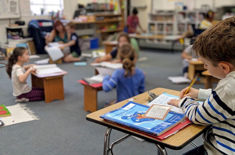 Child writing at a desk in a classroom with other children