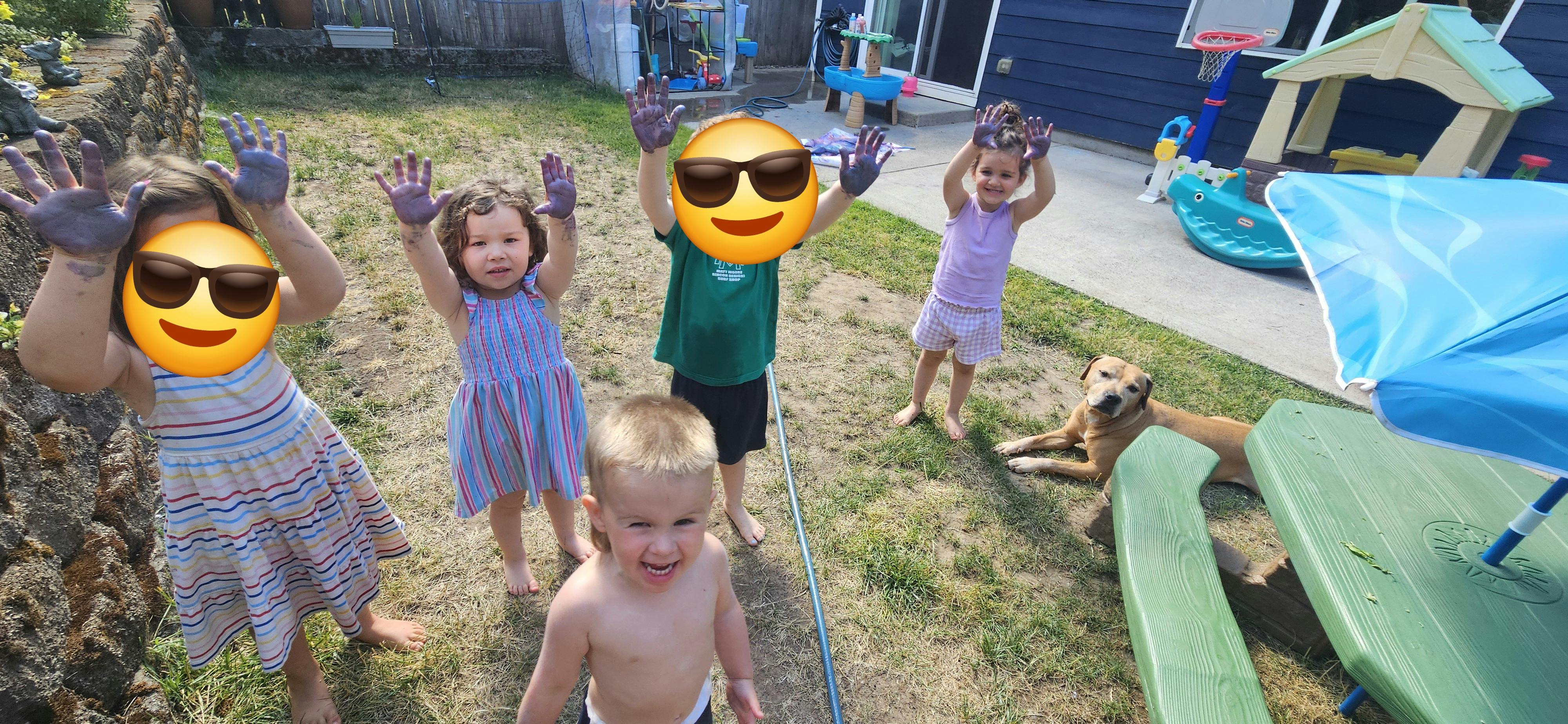 Four children and a dog in a yard, three children with hands raised