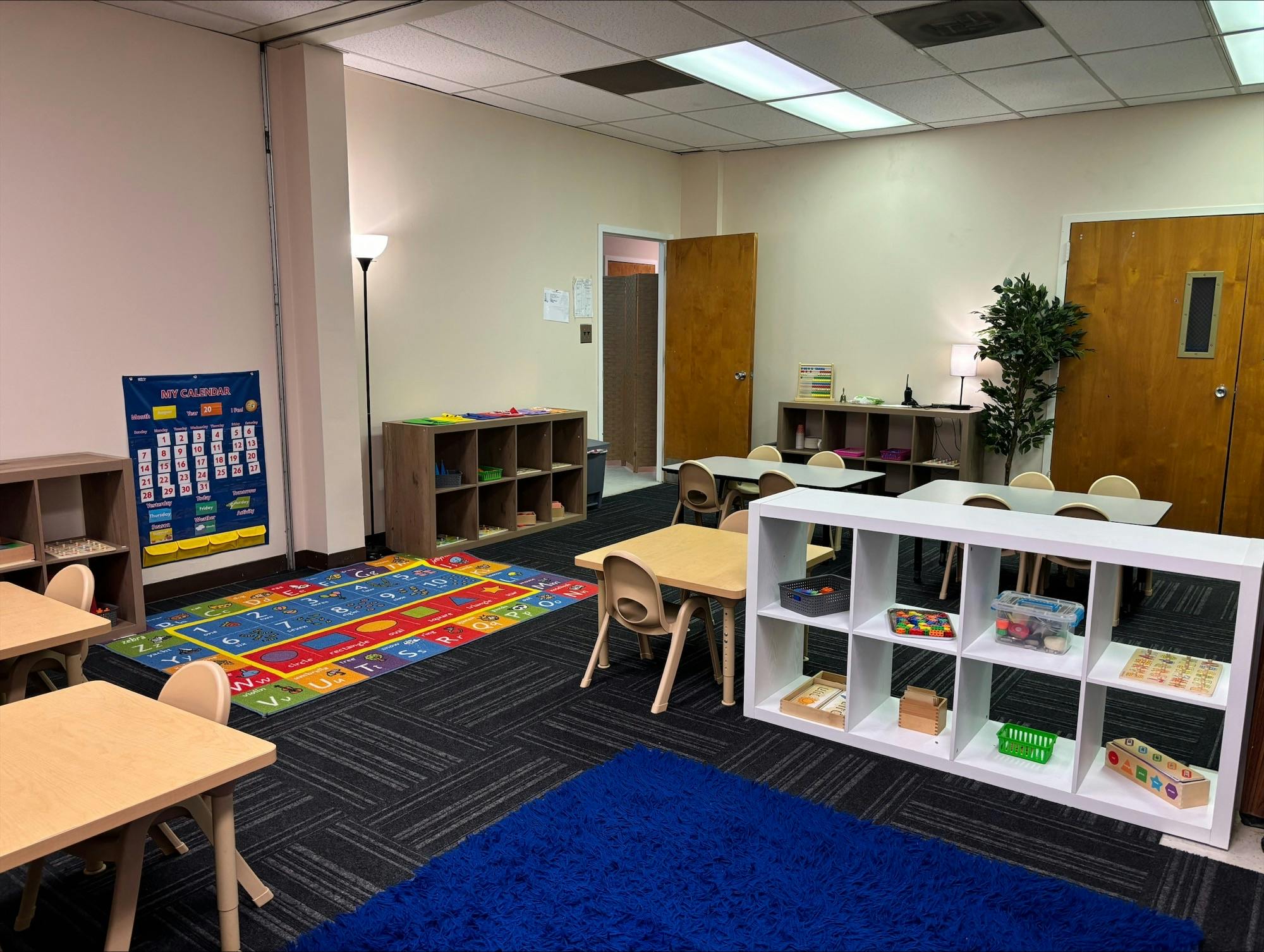 Classroom with small tables and chairs, colorful rugs, and storage shelves