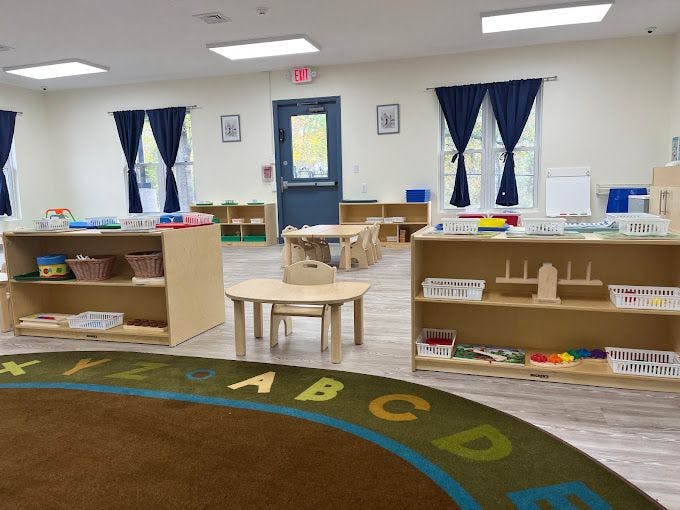 Classroom with child-sized tables and chairs, shelves with learning materials