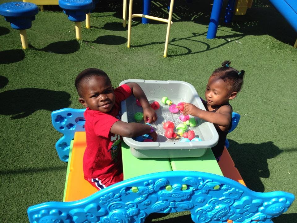 Two children playing with toys in a water table on a playground