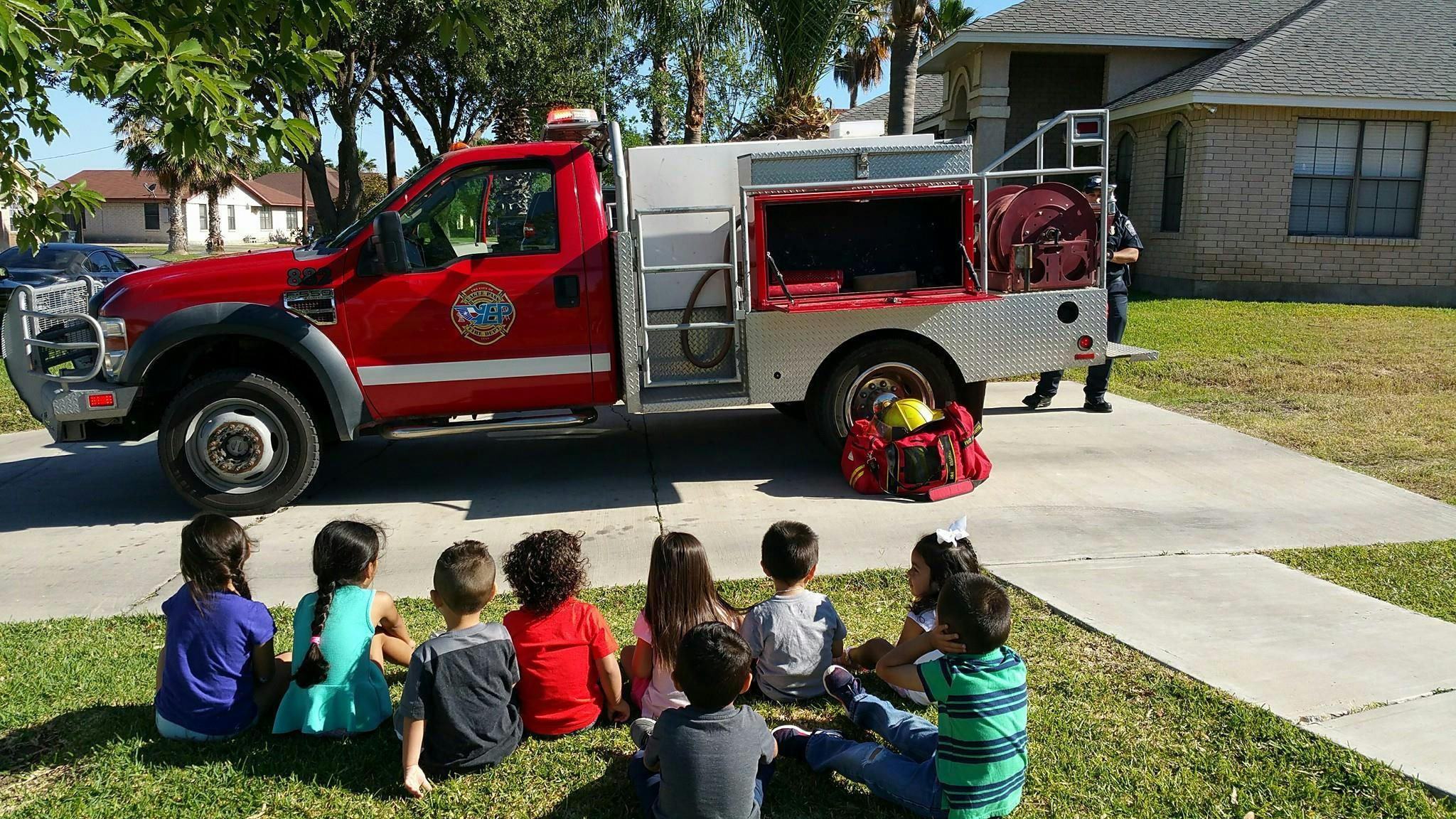 Children sitting on grass looking at a fire truck